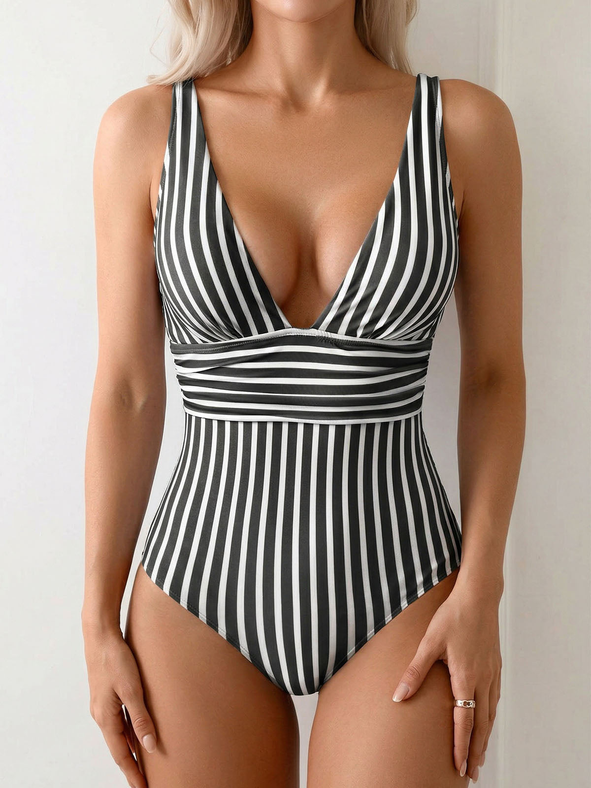 Woman wearing a black and white striped one-piece swimsuit with a deep V-neckline and cinched waist detail.