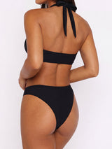 Back view of a woman wearing a black ribbed halter neck bikini top and high-waisted bikini bottoms.