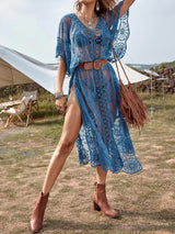 woman wearing a blue sheer lace maxi cover-up with high side slits, belted at the waist and carrying a fringe bag