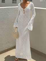 Woman wearing a white open knit maxi dress with bell sleeves and a deep V-neckline, holding a straw handbag.