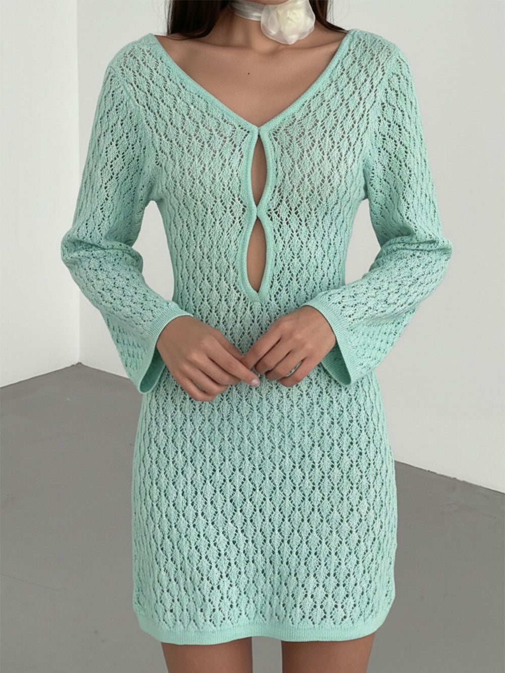 Woman wearing a mint green open knit mini dress with long, flared sleeves and a keyhole neckline.