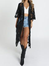 Woman wearing a black lace kimono over a white crop top and denim shorts, with black cowboy boots.