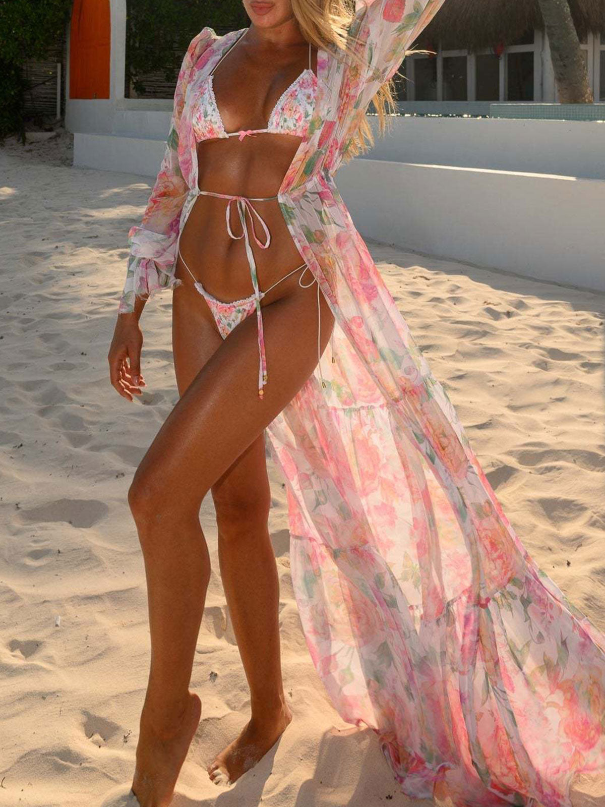 Woman wearing a floral print sheer maxi kimono over a bikini on a sandy beach.