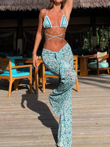 Woman wearing a blue and white printed bikini top with matching high-waisted wide-leg sheer pants, standing on a wooden deck.