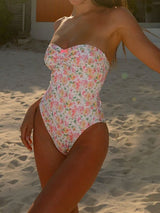 Woman wearing a floral print strapless one-piece swimsuit on a sandy beach.