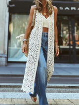 Woman wearing a long, white crocheted lace vest over a crop top and blue jeans
