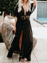 Woman wearing a black sheer maxi cover-up with a V-neck and lace waist detail, holding a patterned tote bag.