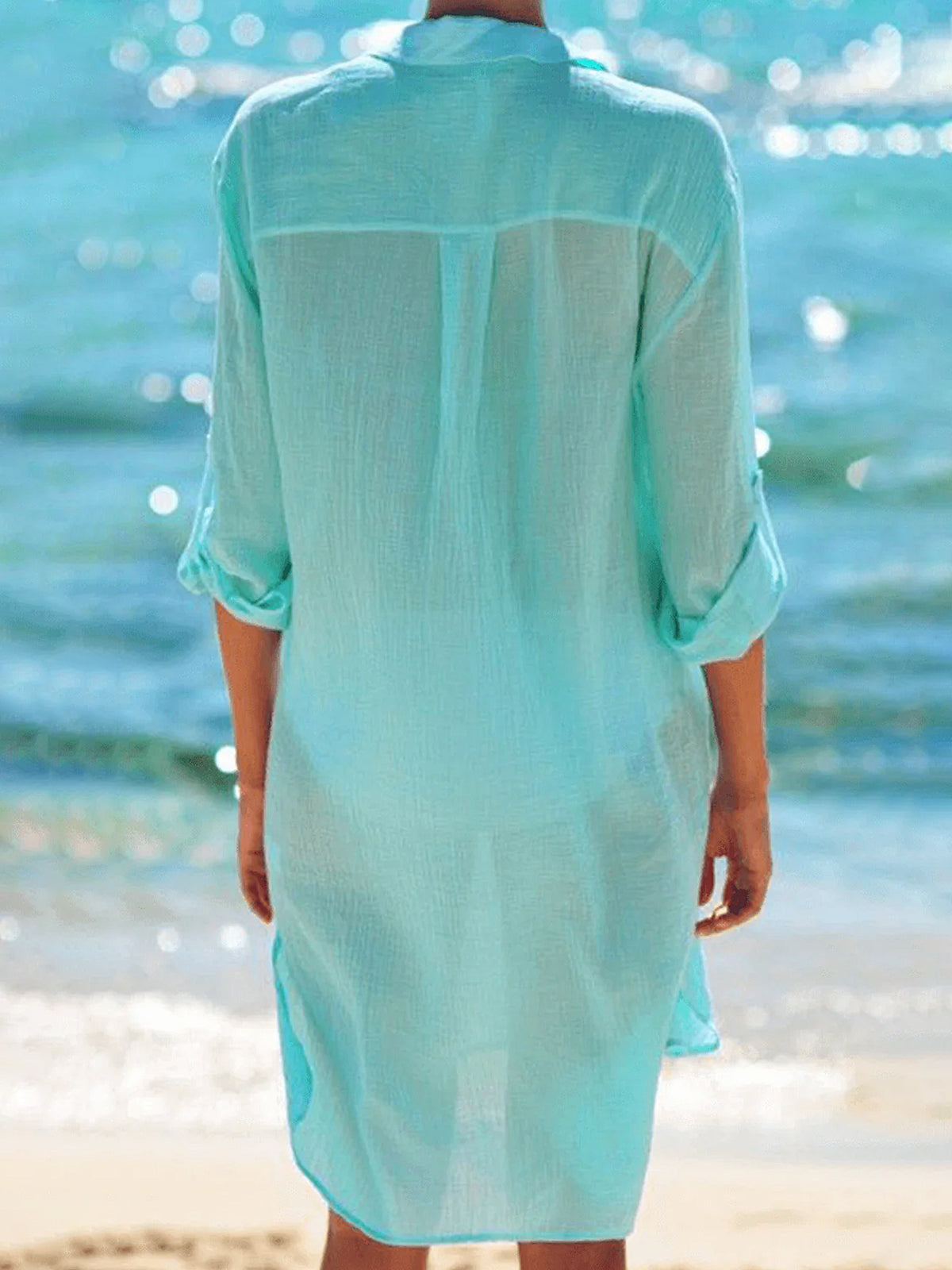 Back view of a woman wearing a light blue sheer button-down tunic at the beach