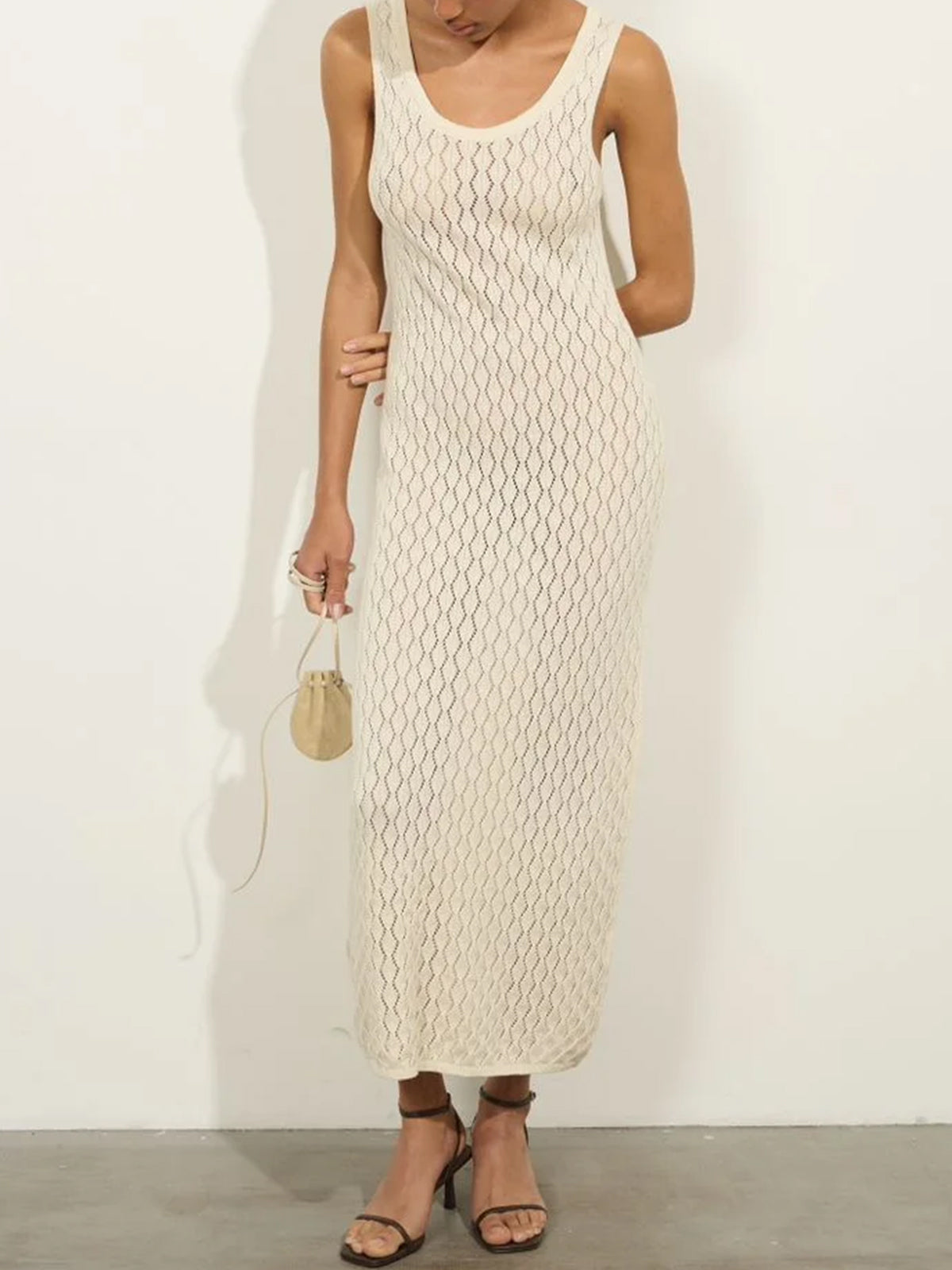 Woman wearing a cream-colored sleeveless maxi knit dress with a scoop neck, holding a small drawstring pouch bag.