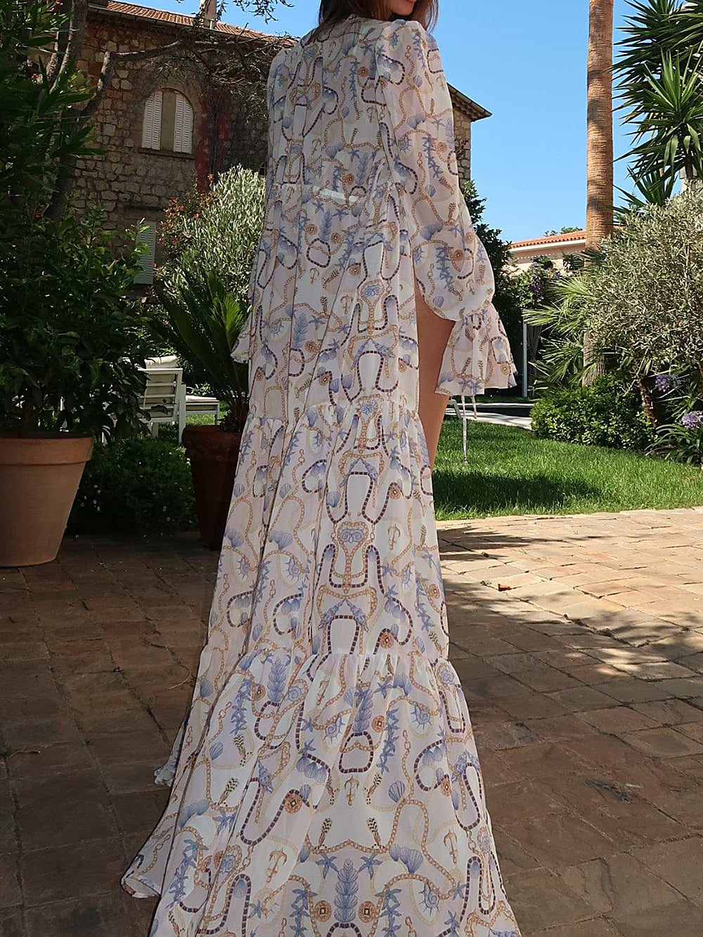 Back view of a woman in a white and blue chain and shell print sheer maxi kimono with a tiered skirt