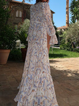 Back view of a woman in a white and blue chain and shell print sheer maxi kimono with a tiered skirt