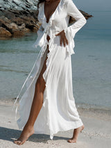 woman in a flowing white maxi dress with ruffled trim and bell sleeves walking on a sandy beach