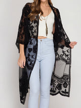 Woman wearing a black lace kimono over a white crop top and light blue jeans.