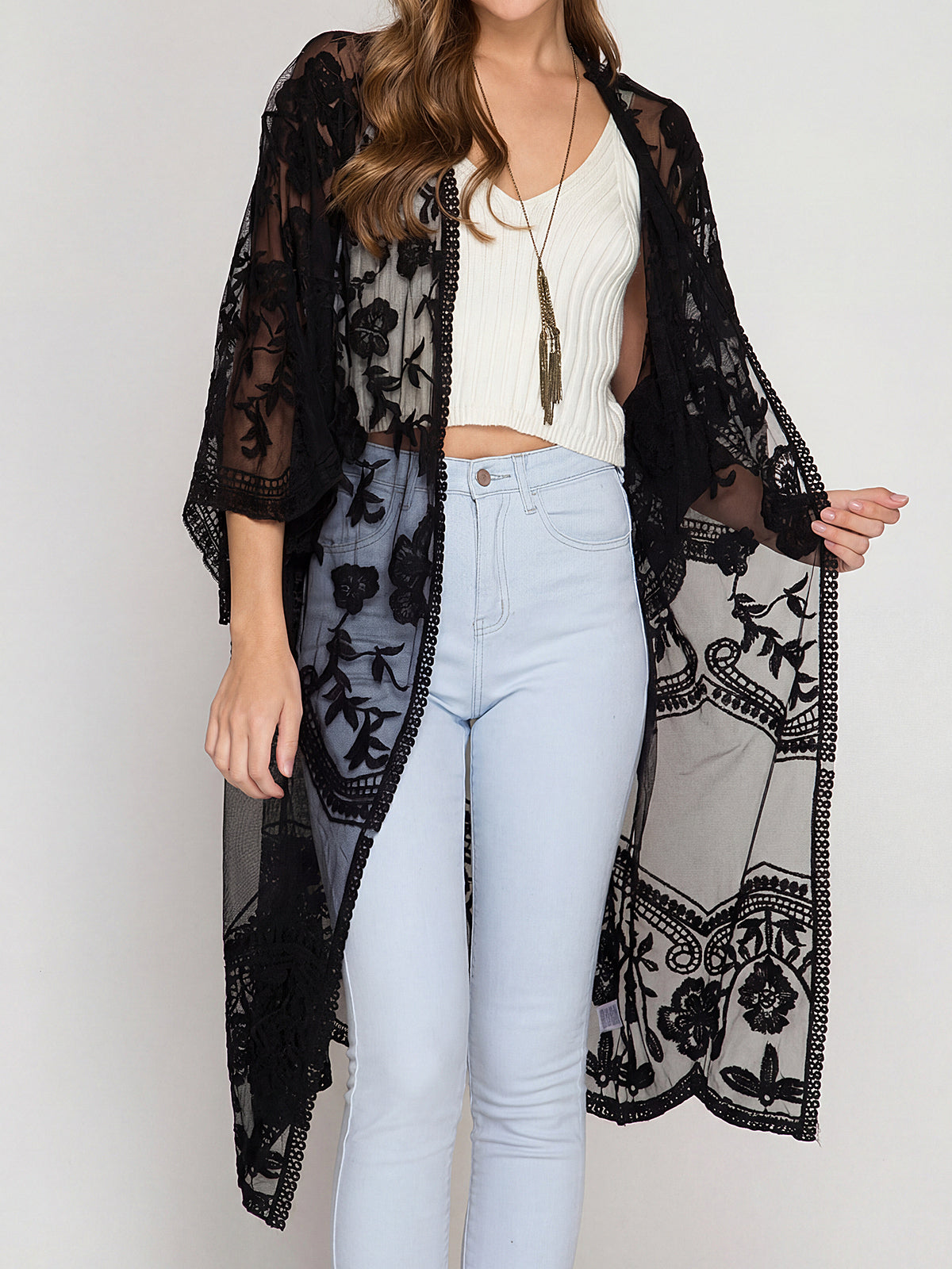 Woman wearing a black lace kimono over a white crop top and light blue jeans.