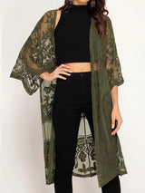 Woman wearing an olive green lace kimono over a black crop top and black jeans.
