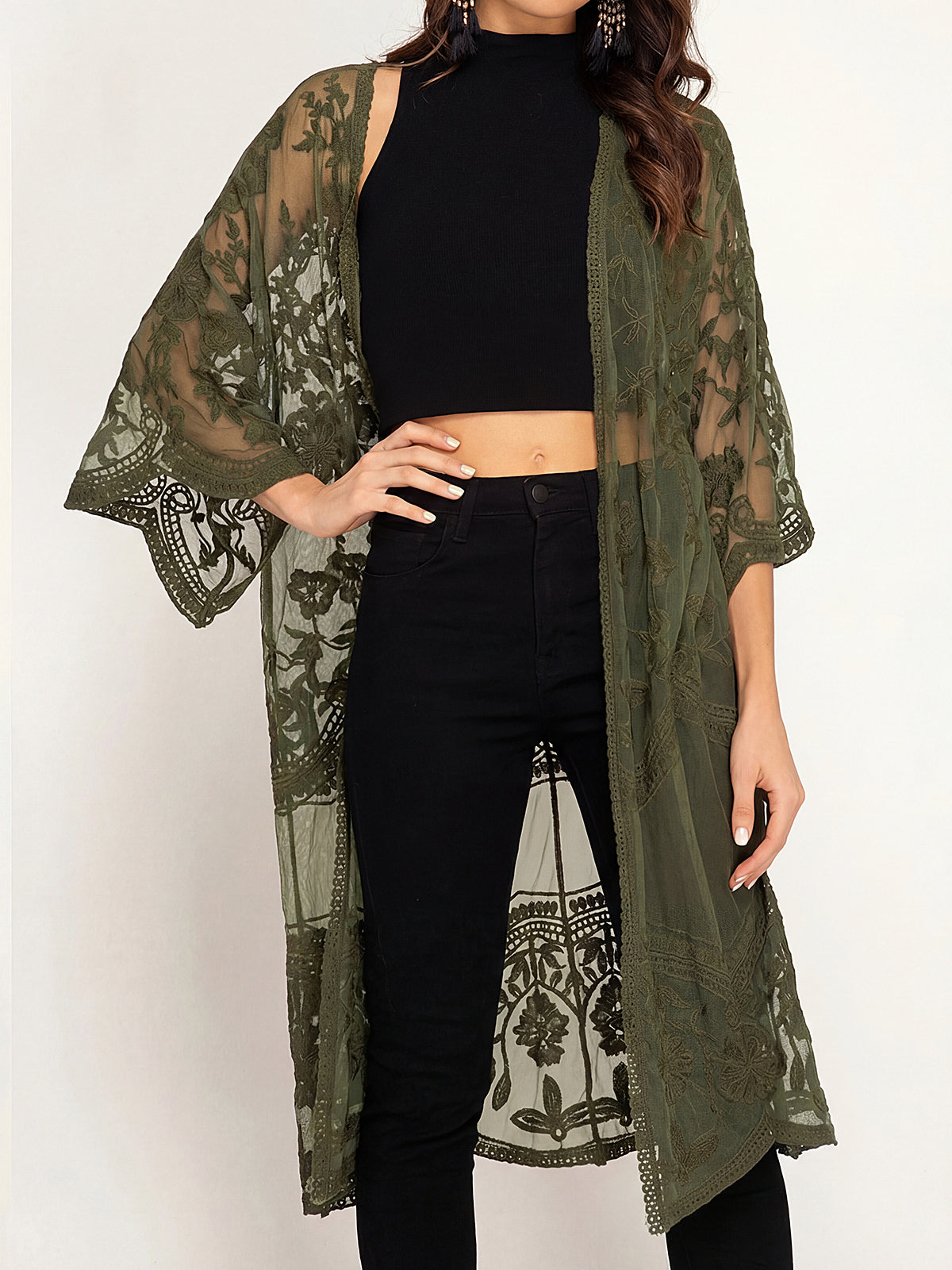 Woman wearing an olive green lace kimono over a black crop top and black jeans.