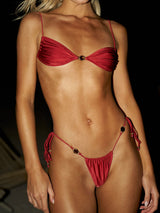 Woman wearing a red shimmering satin bikini with decorative hardware accents and adjustable string ties, front view.