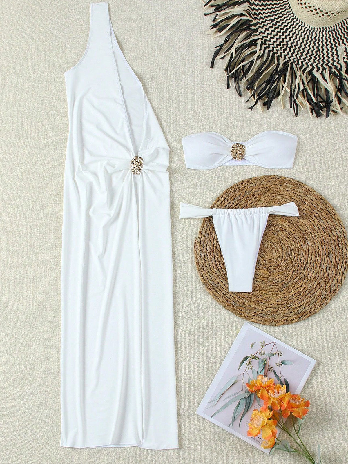 Flat lay of a white one-shoulder maxi dress, white bikini set, straw hat, and decorative items.