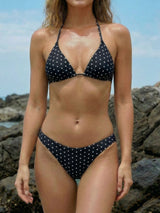 Woman wearing a black and white polka dot bikini on a rocky beach.