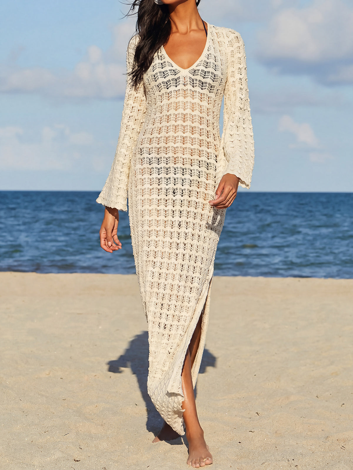 Woman wearing a cream crocheted maxi dress with a v-neck and long bell sleeves on a beach.