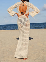 Back view of a woman in a cream crocheted maxi dress with an open back and tie detail.