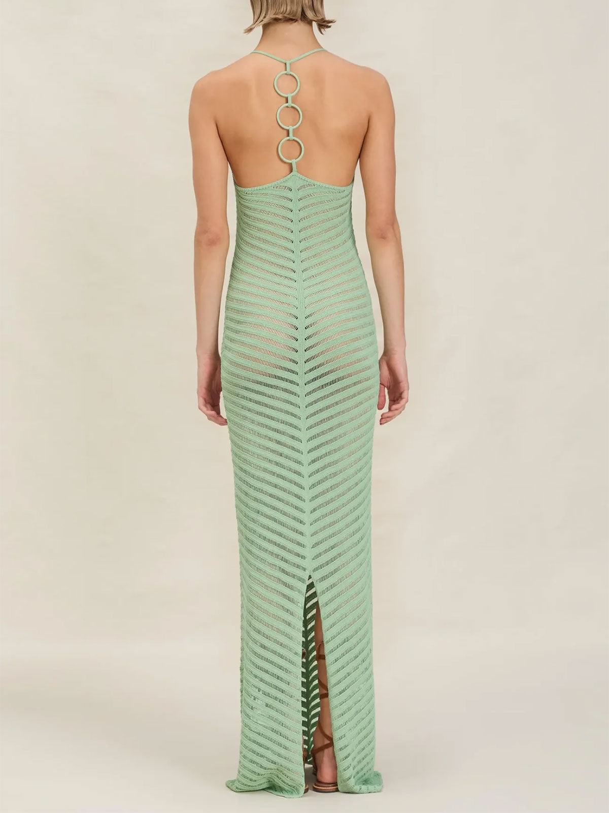 back view of woman wearing a long, light green, chevron-patterned knit halter dress with an open back detail