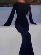 Woman in a black long-sleeved maxi dress with a matching handbag.