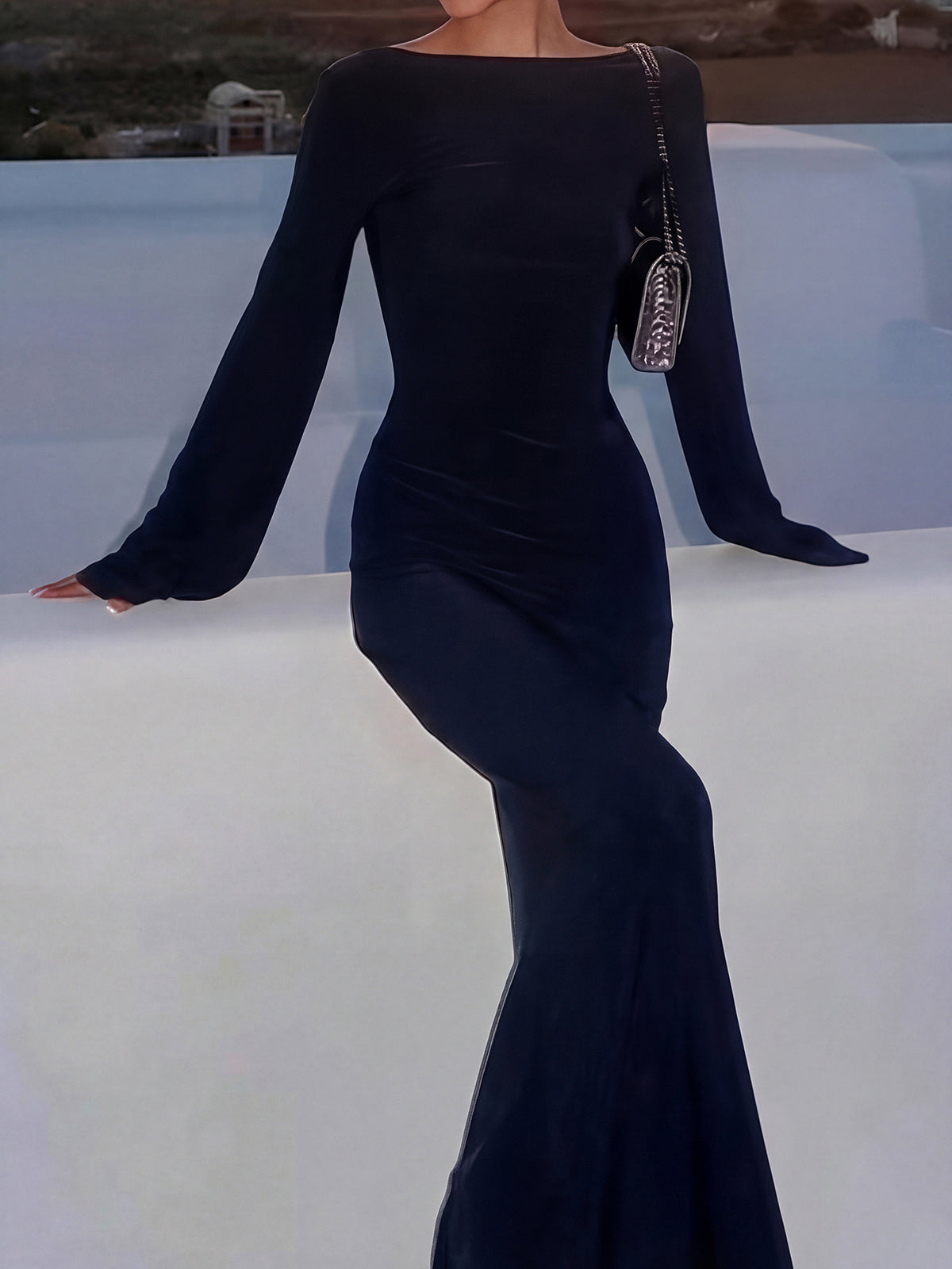 Woman in a black long-sleeved maxi dress with a matching handbag.