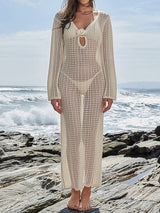 Woman in a cream crochet maxi dress with long sleeves, standing on a rocky shore.