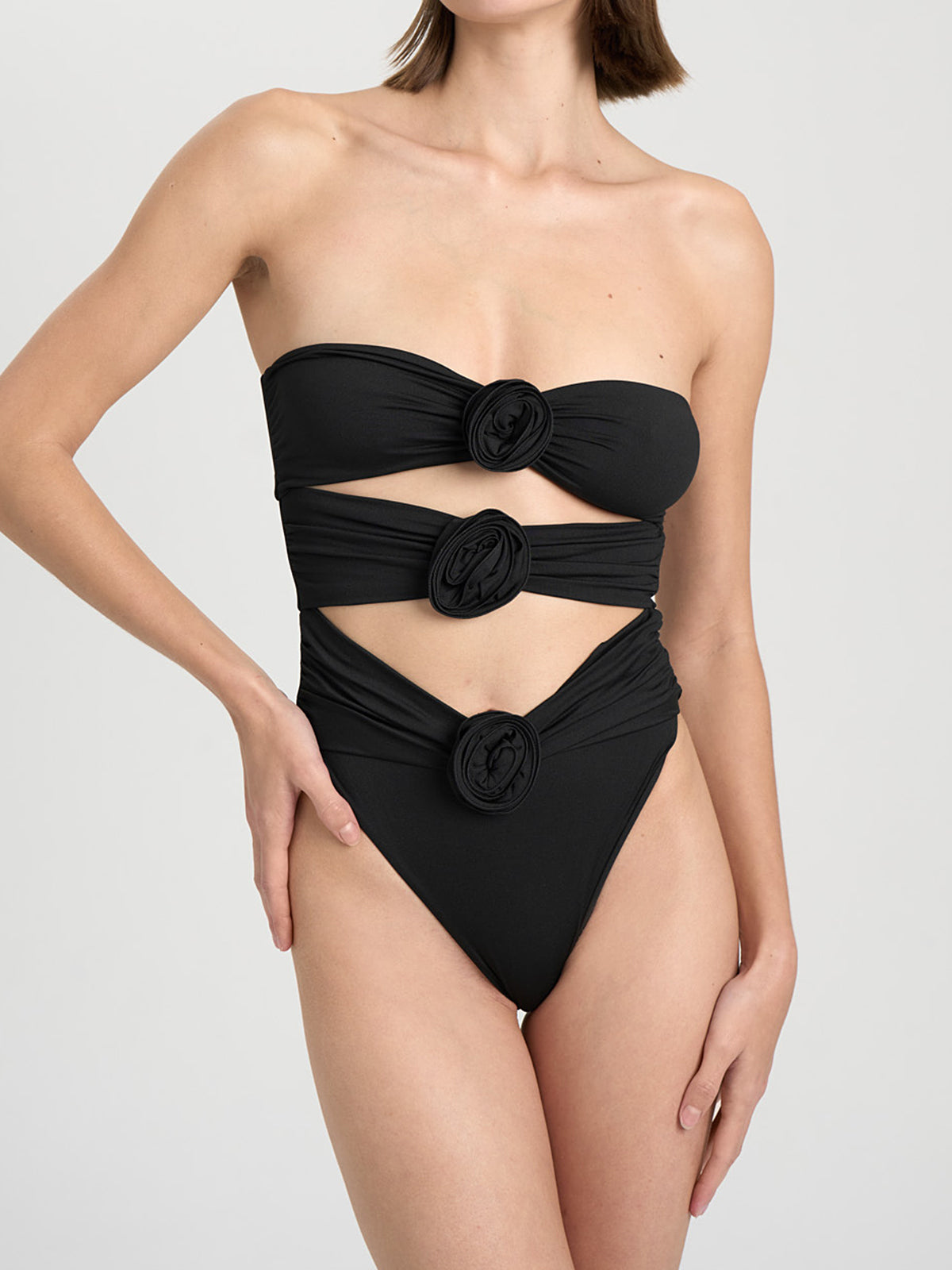 Woman wearing a black strapless one-piece swimsuit with cut-out details and floral embellishments, front view.