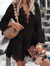 Woman wearing a black lace tunic over a swimsuit, holding a woven bag and sandals.