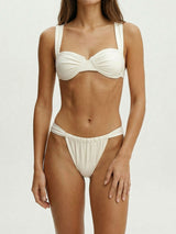 Woman wearing a white ruched bikini top with wide shoulder straps and high-cut bikini bottoms with side ties