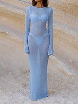 Woman wearing a light blue sheer knit maxi dress over a light blue bikini on a sandy beach