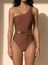 Front view of a woman wearing a brown one-shoulder one-piece swimsuit with a belted waist.