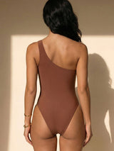 Back view of a woman wearing a brown one-shoulder one-piece swimsuit.