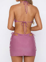 Back view of a woman wearing a mauve halter bikini top and matching ruched mini skirt.