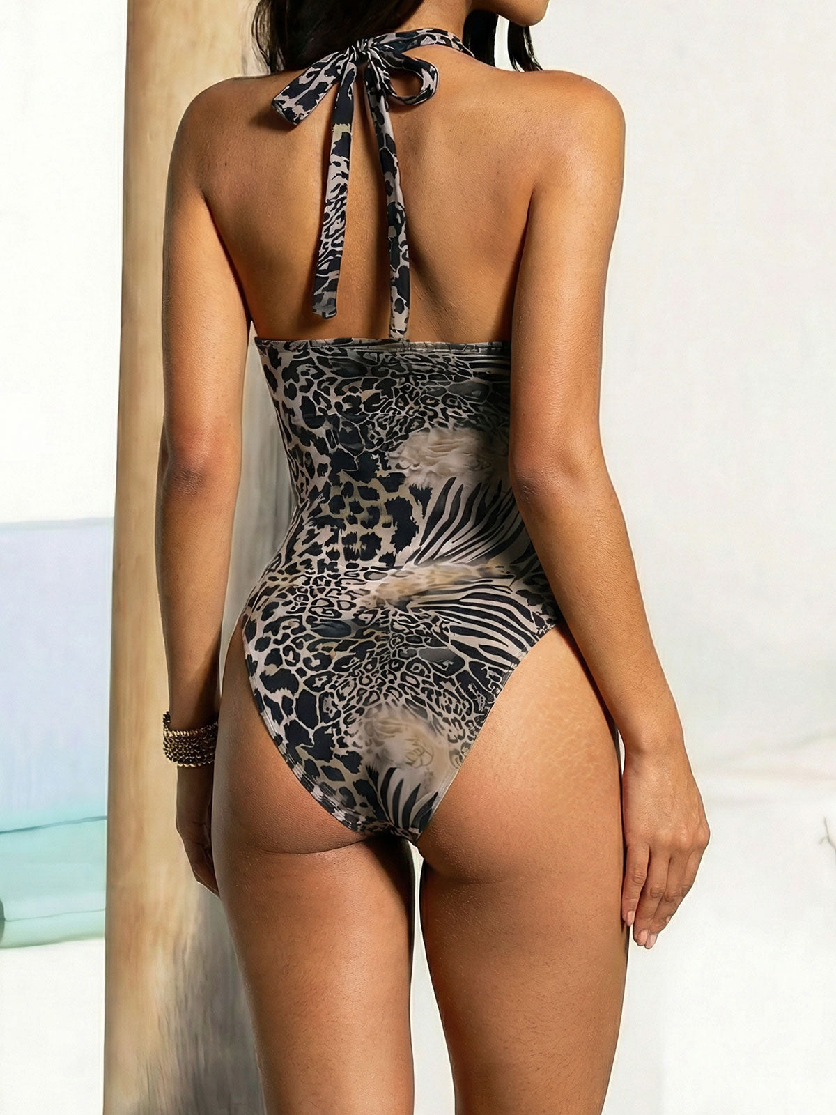 Back view of a woman wearing a one-piece swimsuit with a halter neck.